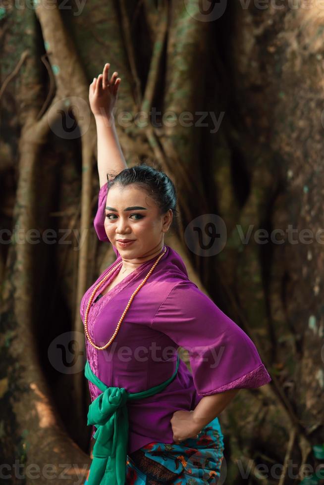 An Indonesian woman bravely poses while raising her hands in a purple dress photo