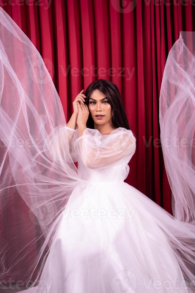 Elegance Asian woman wearing a wedding dress with flying fabric around her in front of the red curtain photo