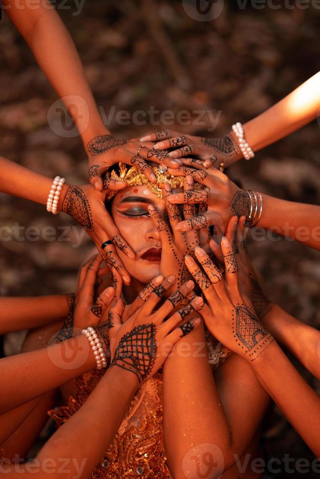 Sad Man Faces covered up by a lot of hands with henna tattoos while wearing a gold crown photo