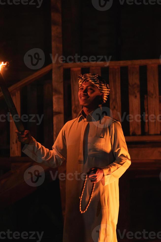 An Arabian man holding a fire torch in the front of a wooden house photo