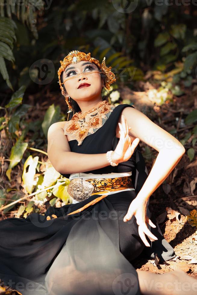 Indian woman sitting with a black dress and makeup on her face while wearing a golden crown and golden necklace on her body photo