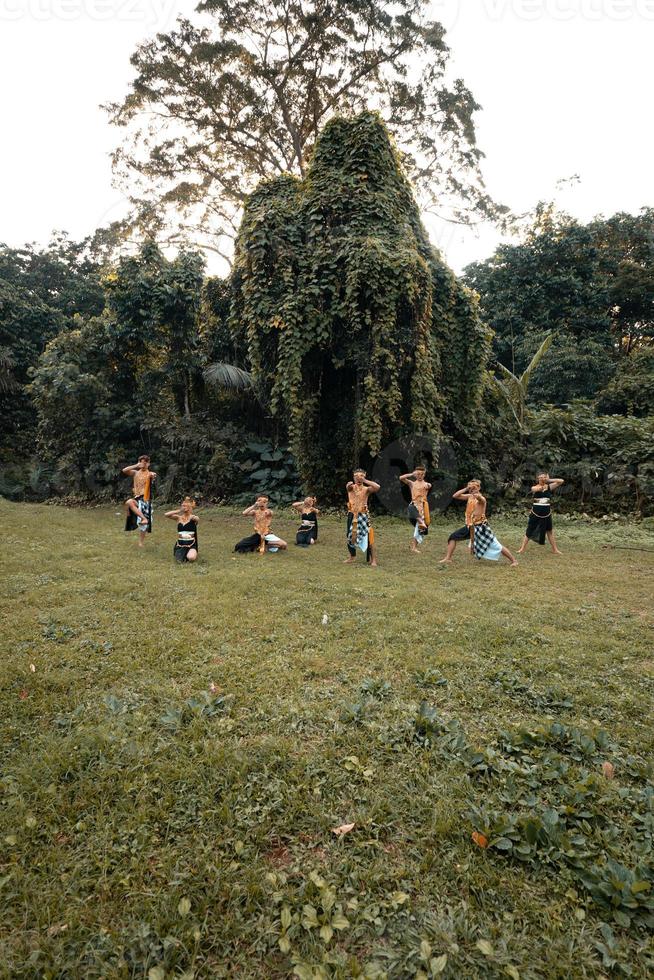 A Group of Asian people with golden dance costumes pose on the green grass in front of the jungle photo