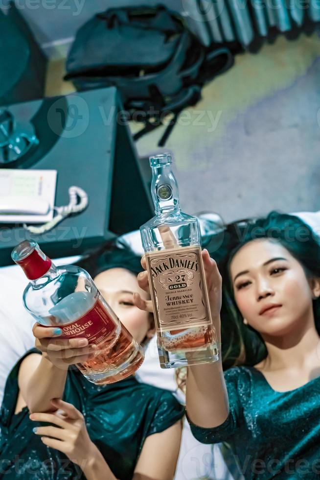 Asian women holding an alcohol bottle in their hand in the bedroom photo