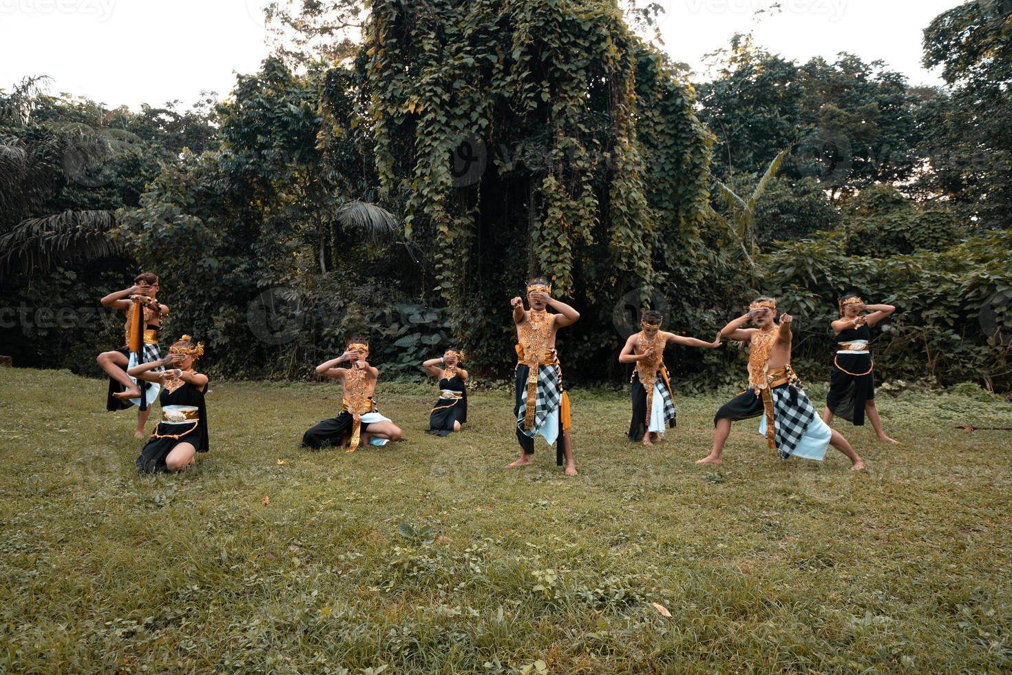 A Group of Asian people with golden dance costumes pose on the green grass in front of the jungle photo