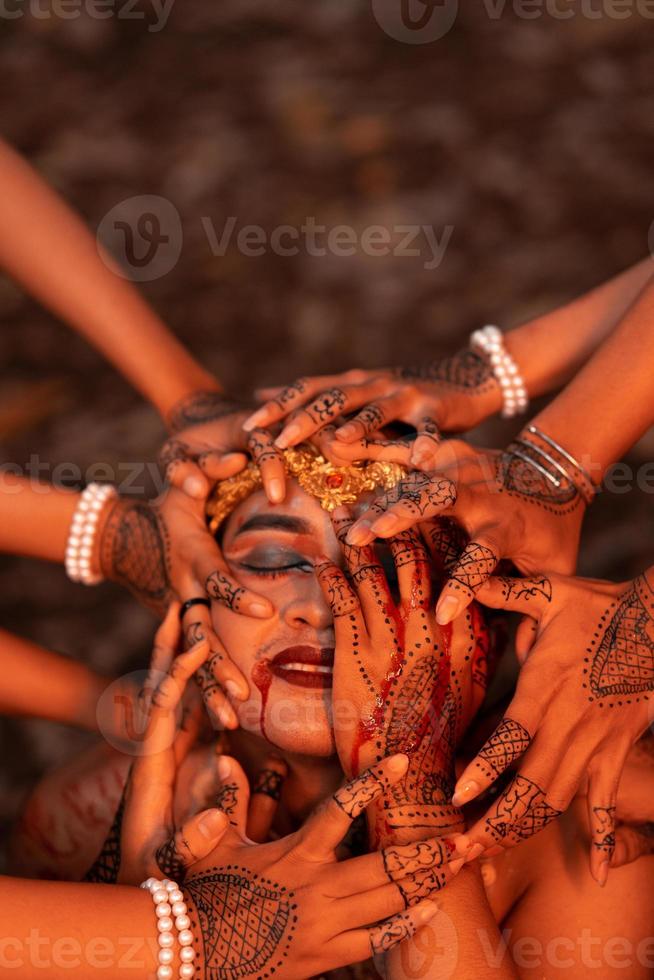 A Lot of hands holding an Asian man's face who had fake blood on her red lips like he was in pain photo