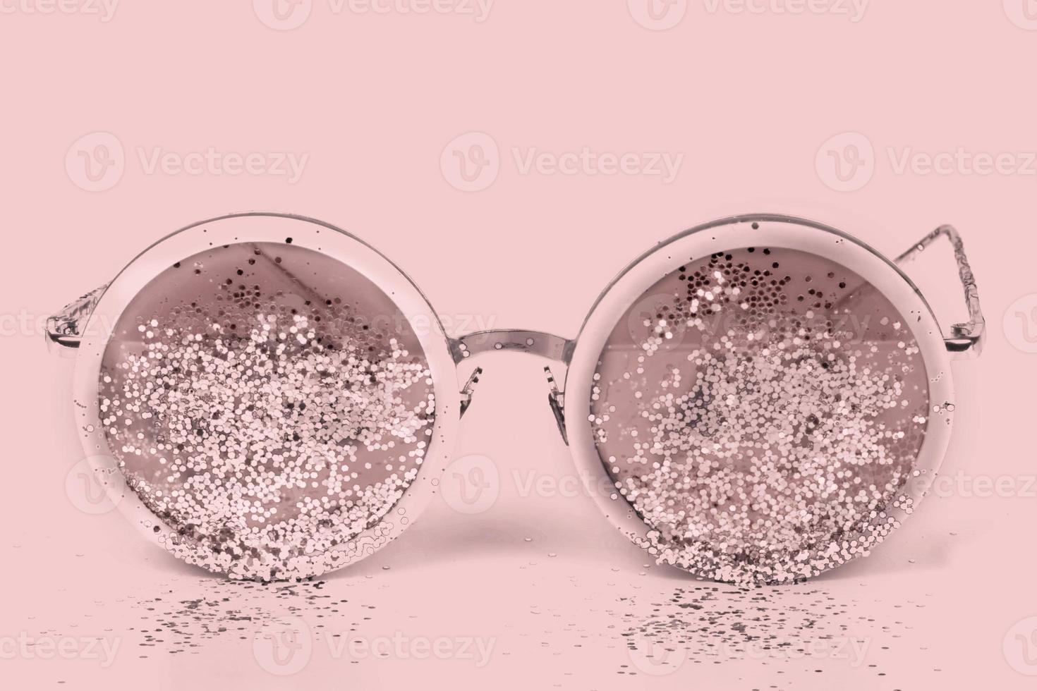 Pink sunglasses with sparkles on a pink background. photo