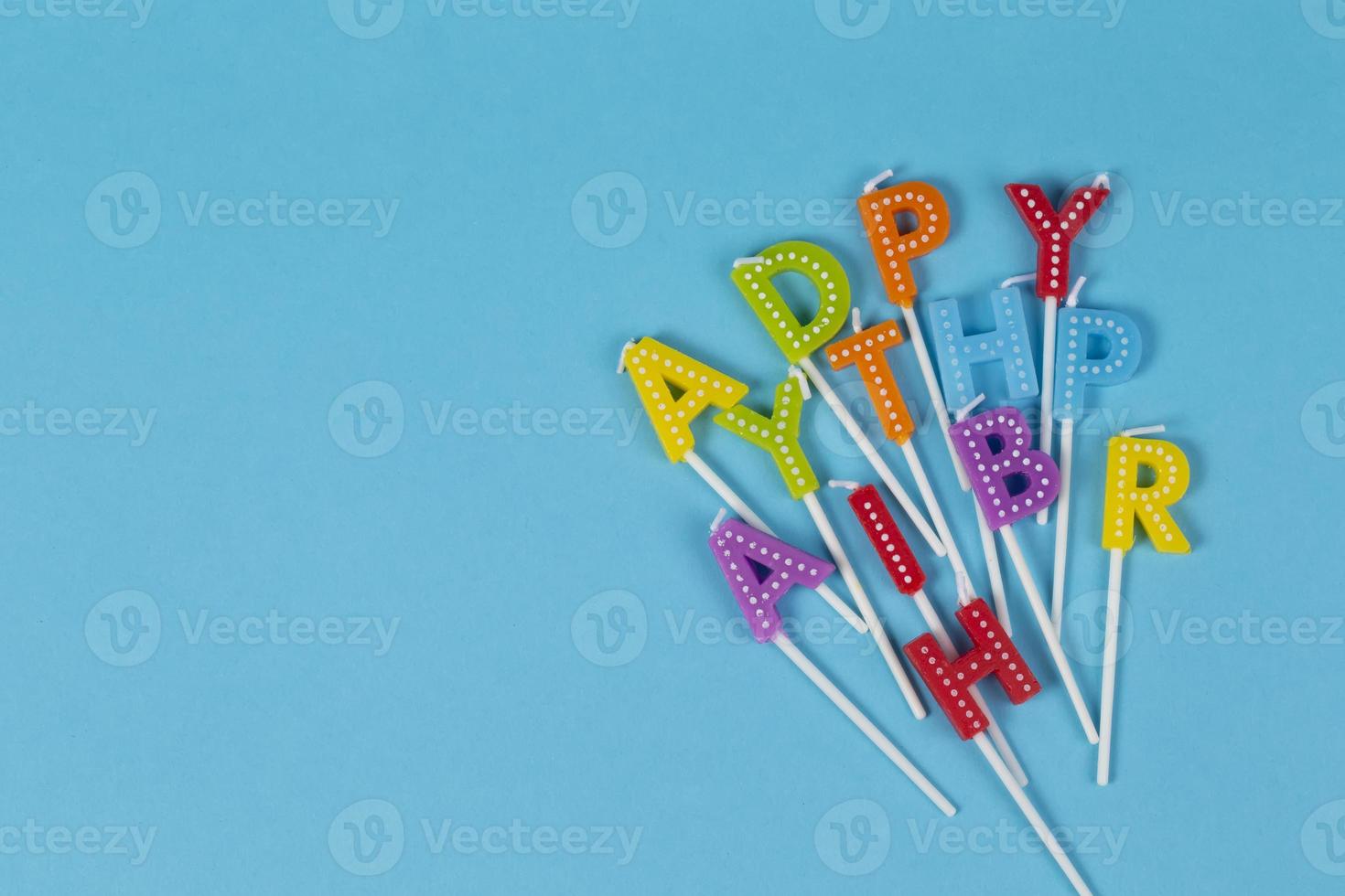Colorful candles in letters with  Happy Birthday  lettering isolated on blue background.Happy birthday letters mixed up. photo