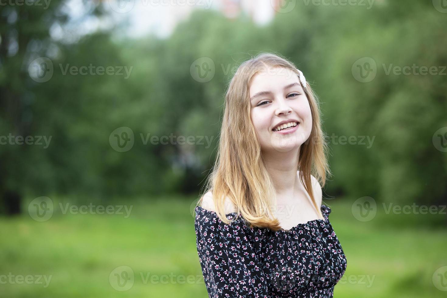 Happy young girl in a romantic dress on a green summer meadow. Beautiful teen girl smiles and looks into the camera. photo