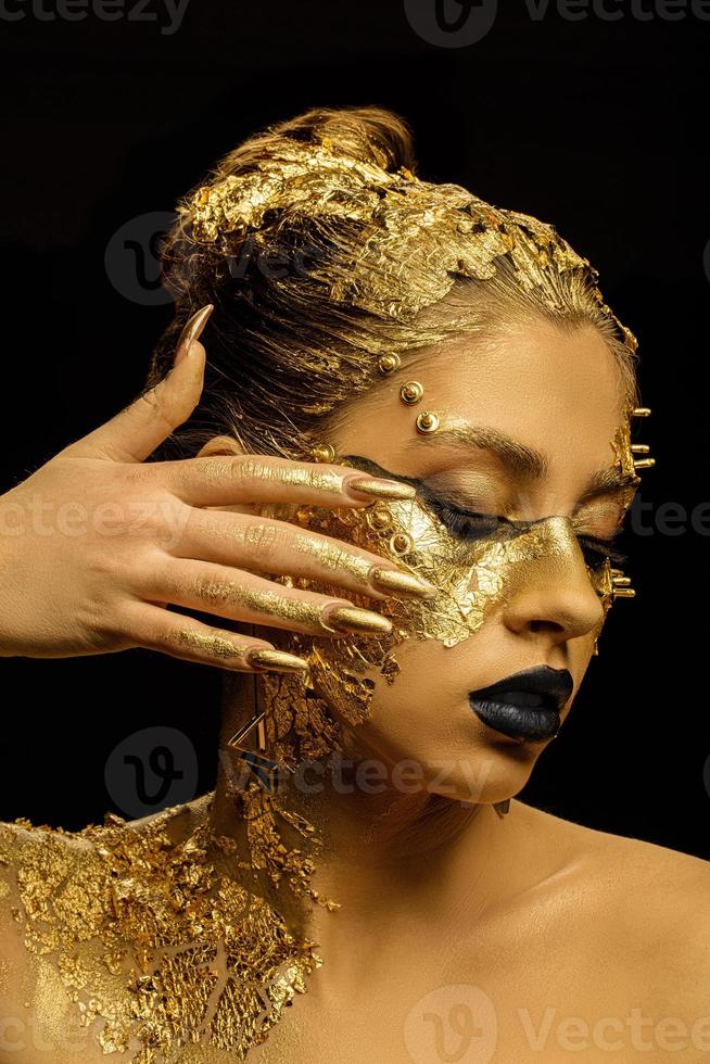 Fashion art Golden skin. Model girl with festive golden glamorous shiny professional make-up. Gold jewelry, bijouterie, accessories. Beautiful golden metallic body, black lips and skin. photo