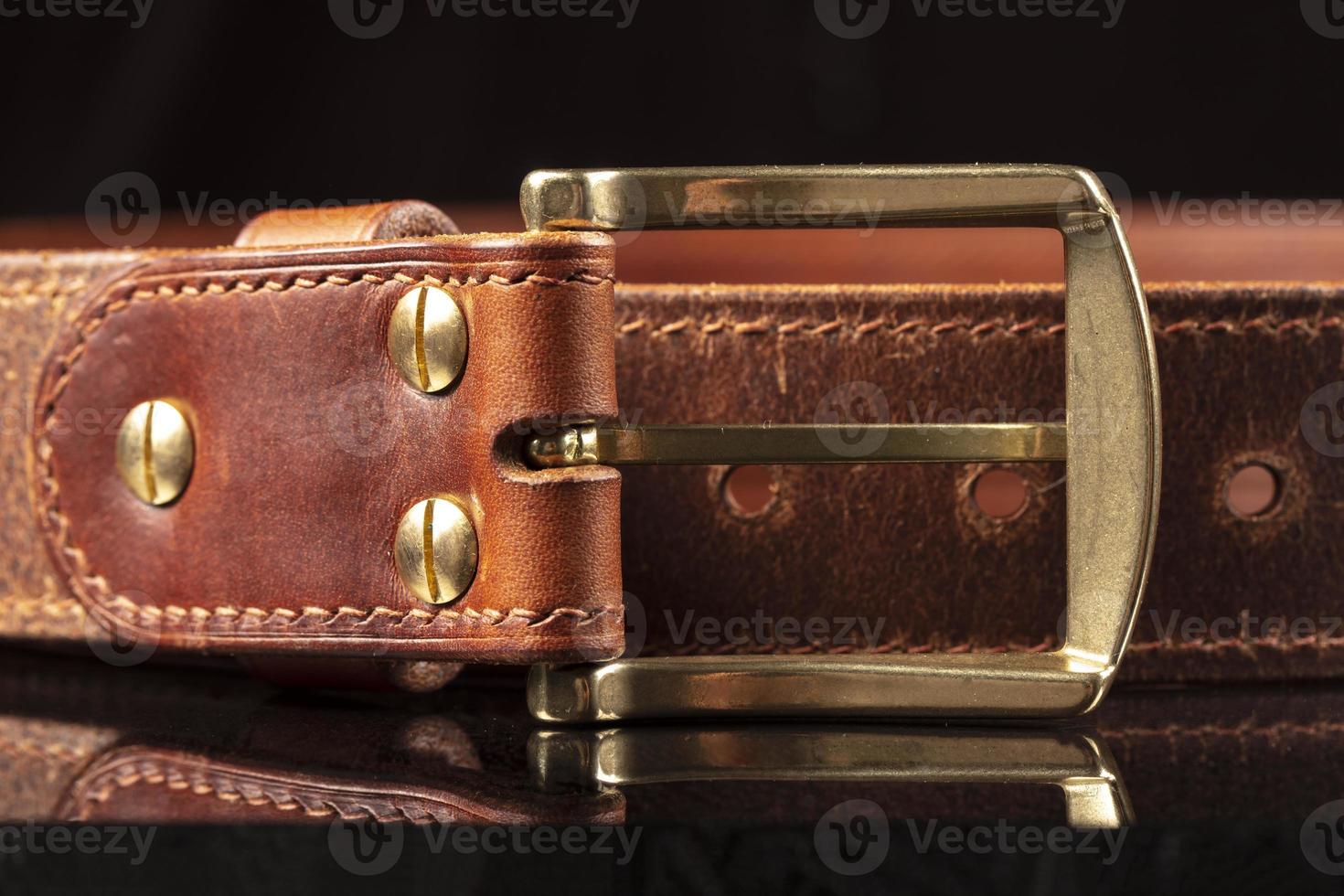 Part of a leather brown belt with a metal buckle on a black background. photo
