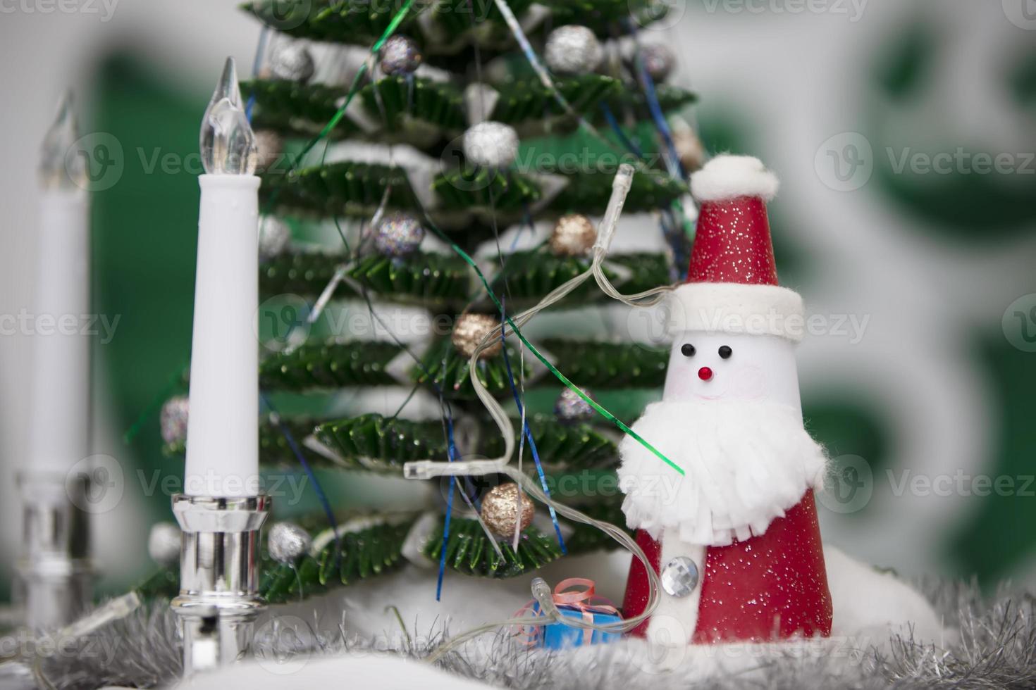 A toy santa claus stands near a decorated small Christmas tree. photo
