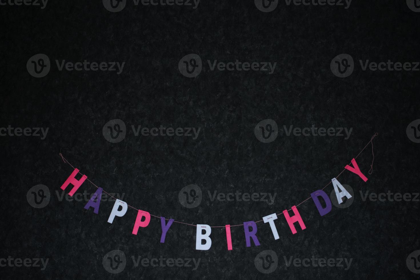 Multicolored garland of letters Happy birthday on a dark background. photo