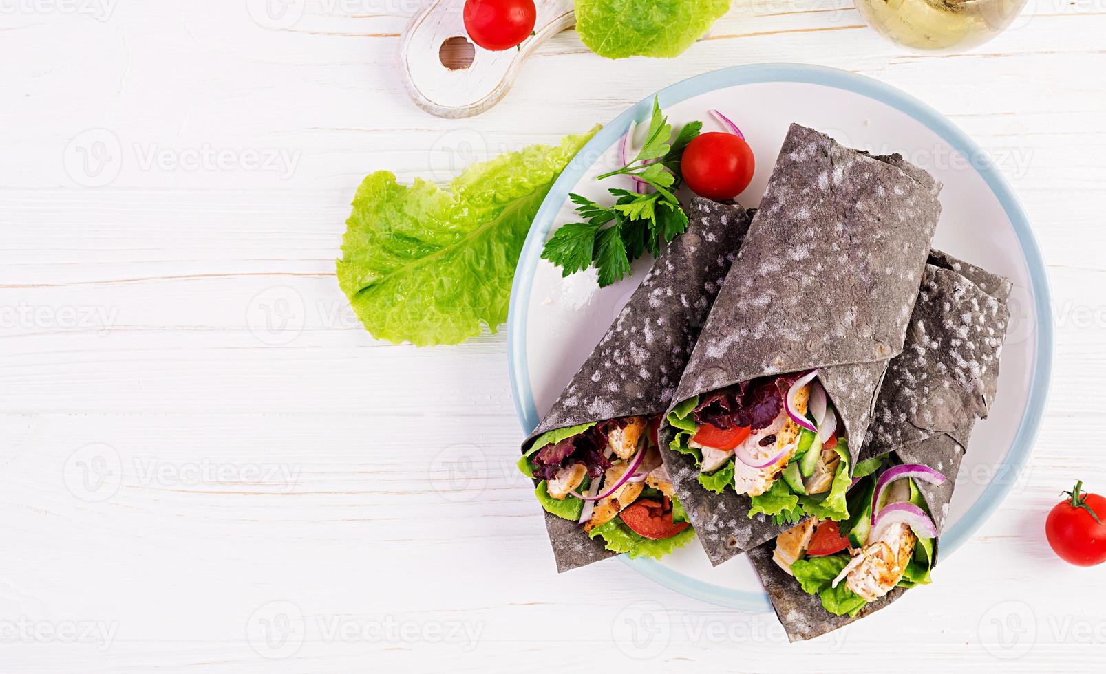 Tortilla with added ink cuttlefish wraps with chicken and vegetables on white background. Chicken burrito, mexican food. Top view photo
