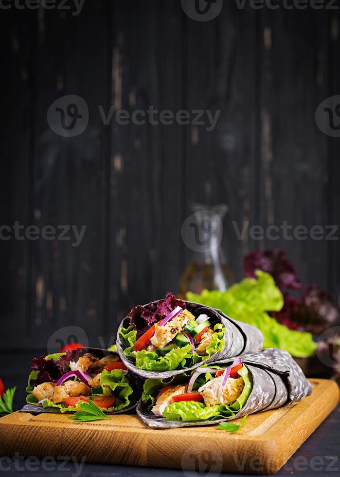 tortilla con tinta añadida envolturas de sepia con pollo y verduras sobre fondo negro. burrito de pollo, comida mexicana. foto