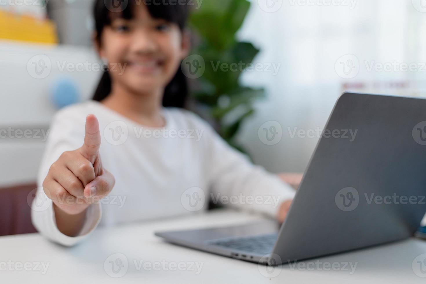 colegiala asiática haciendo su tarea con una laptop en casa. los niños usan aparatos para estudiar. educación y aprendizaje a distancia para niños. educación en el hogar durante la cuarentena. Quédate en casa foto