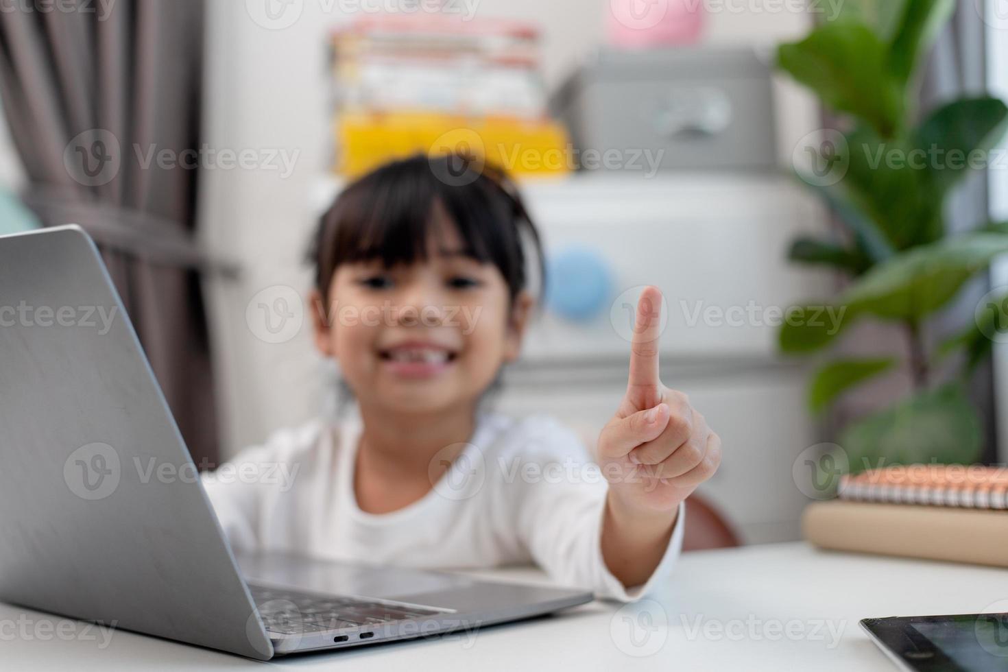 colegiala asiática haciendo su tarea con una laptop en casa. los niños usan aparatos para estudiar. educación y aprendizaje a distancia para niños. educación en el hogar durante la cuarentena. Quédate en casa foto