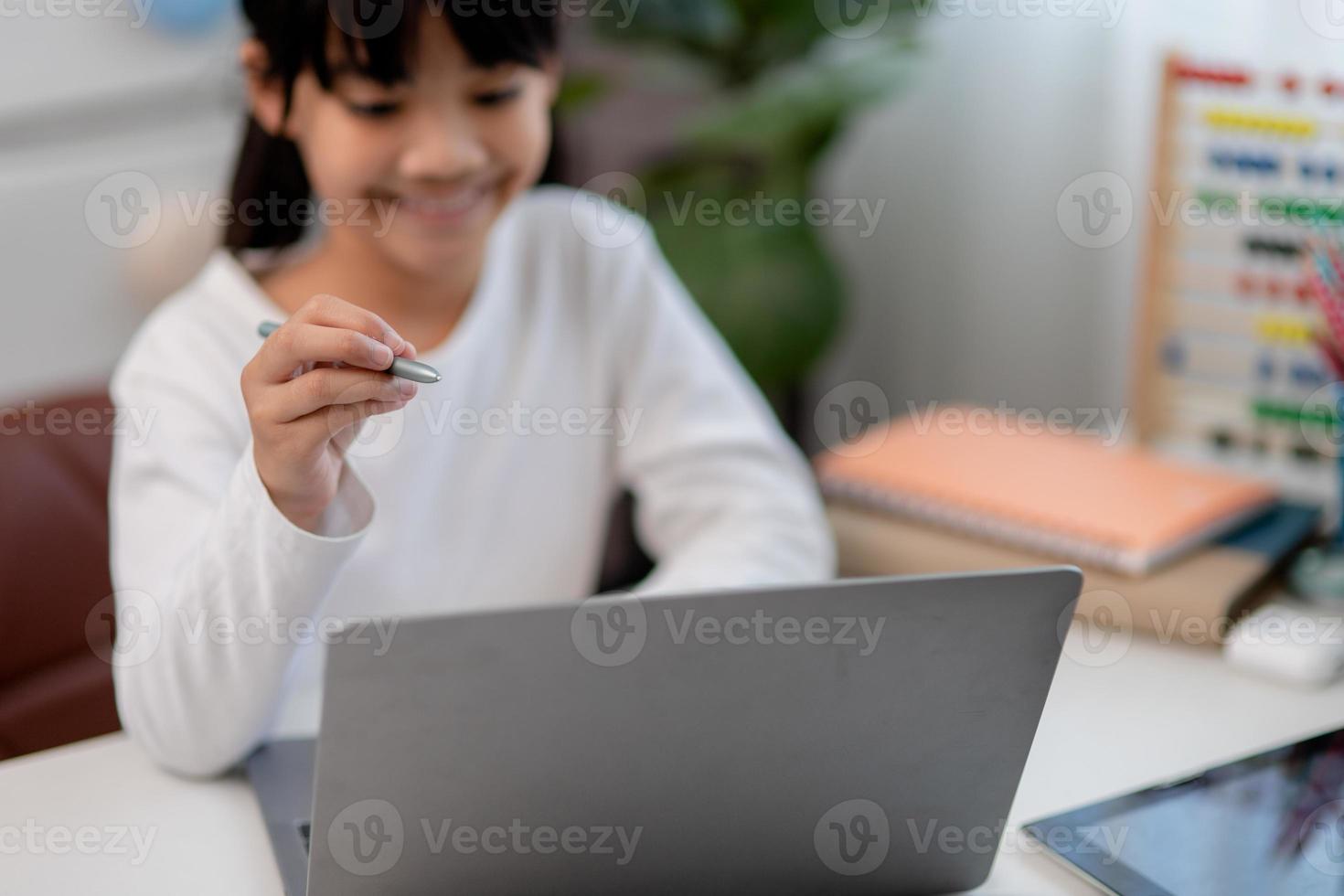Asian schoolgirl doing her homework with laptop at home. Children use gadgets to study. Education and distance learning for kids. Homeschooling during quarantine. Stay at home photo