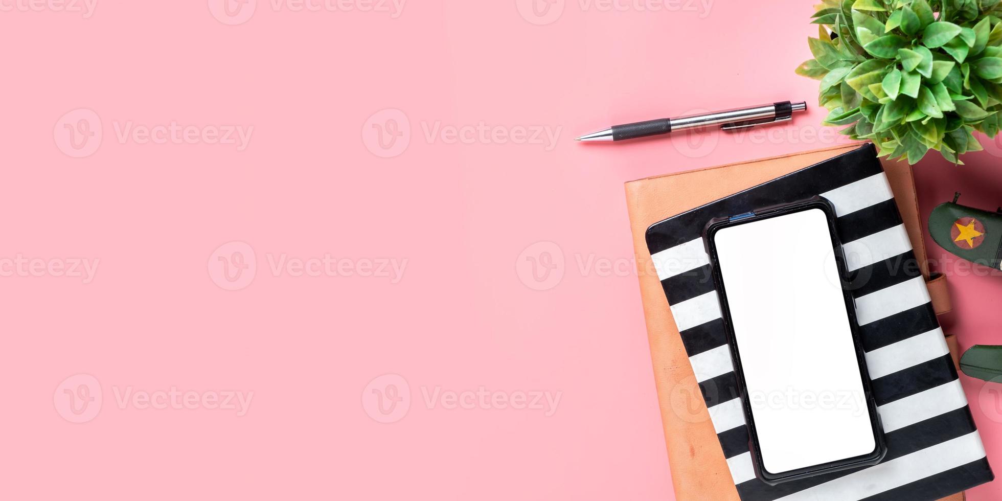 Office desk with Blank screen smart phone, Pen, Notebook, Cup of coffee on pink background, Top view with copy space, Mock up. photo