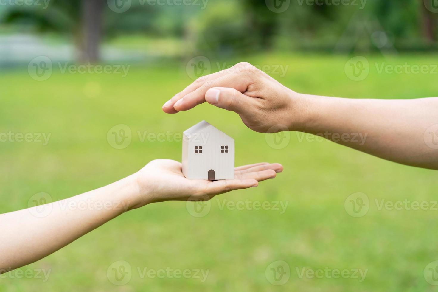 Close-up of couple hand holding wooden house model with green natural and sunlight background photo