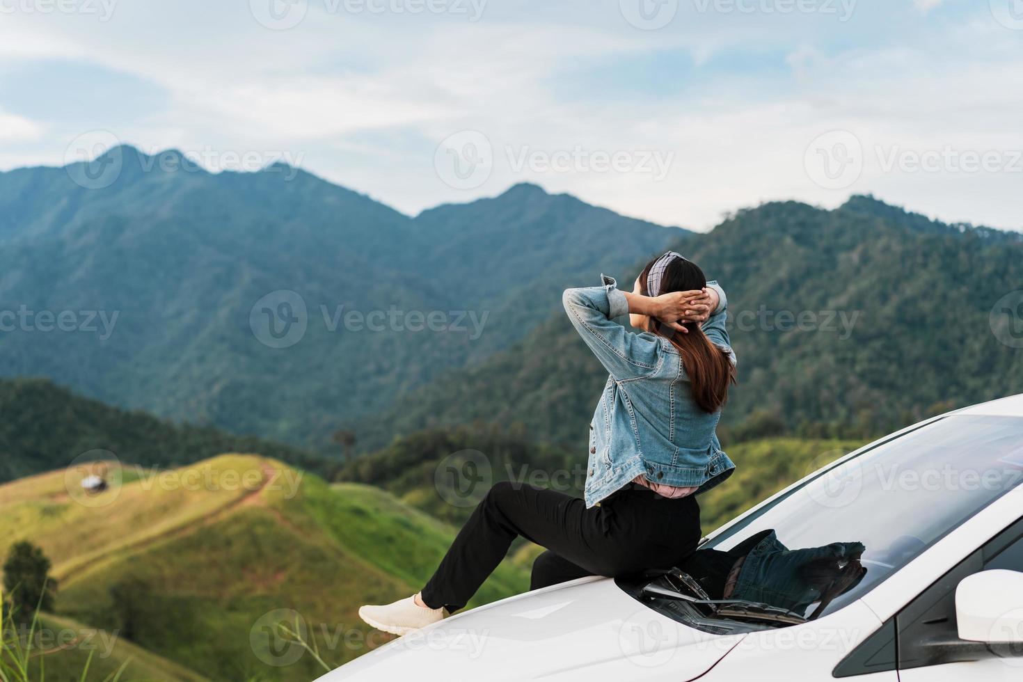 Young woman traveler sitting on a car watching a beautiful mountain view while travel driving road trip on vacation photo