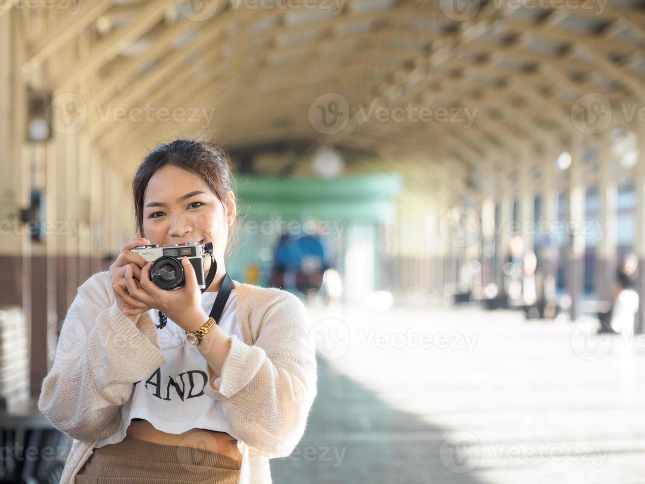 jovencita mujer asiática hermoso cabello largo y fresco con camisa blanca modelo con cámara de película retro de pie en la estación de tren de bangkok, viaje de vacaciones durante el día de la tarde foto