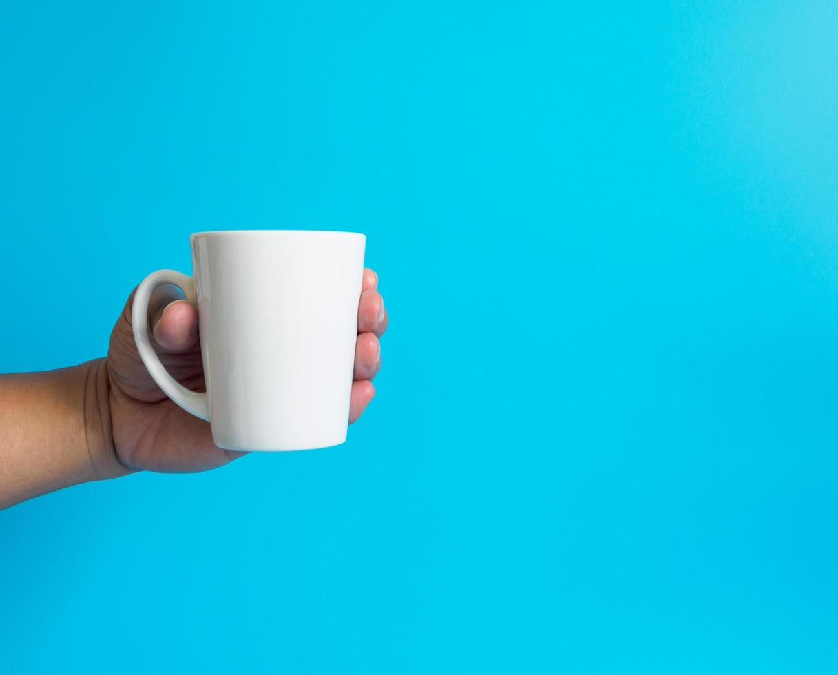 Man hand holding a white coffee cup, filled with hot black coffee americano, no sugar no milk, ready to drink, refreshing. aroma awake fresh to work placed on a blue isolated background photo