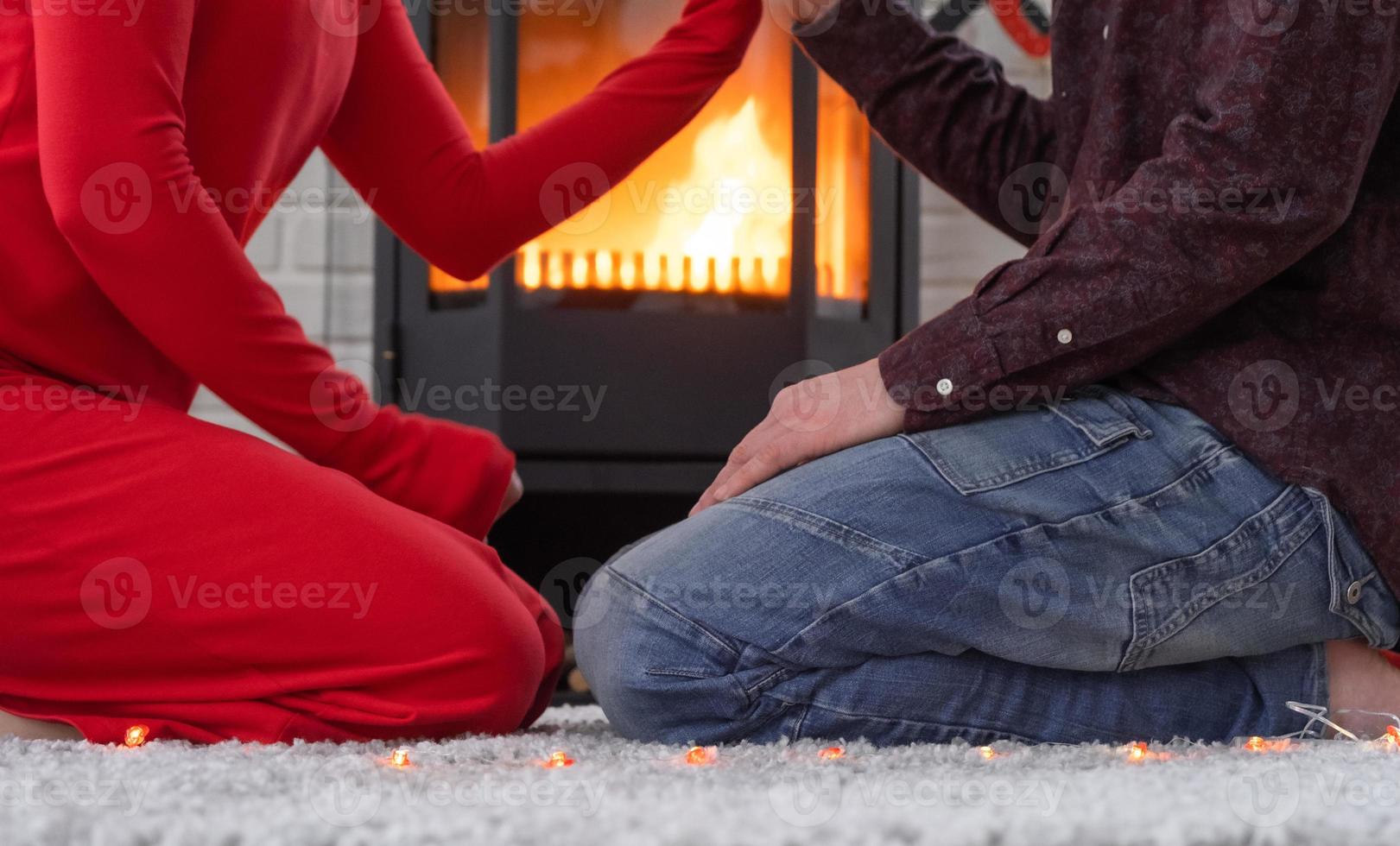 el hombre y la mujer enamorados en casa están sentados cerca de la estufa de la chimenea con un fuego ardiente en una alfombra acogedora. día de san valentín, pareja feliz, historia de amor, relaciones foto