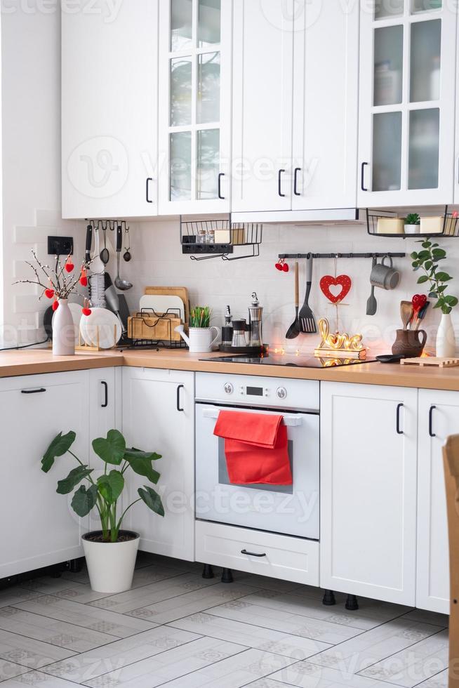 The interior of the kitchen in the house is decorated with red hearts for Valentine's Day. Decor on the table, stove, utensils, festive mood in a family nest photo