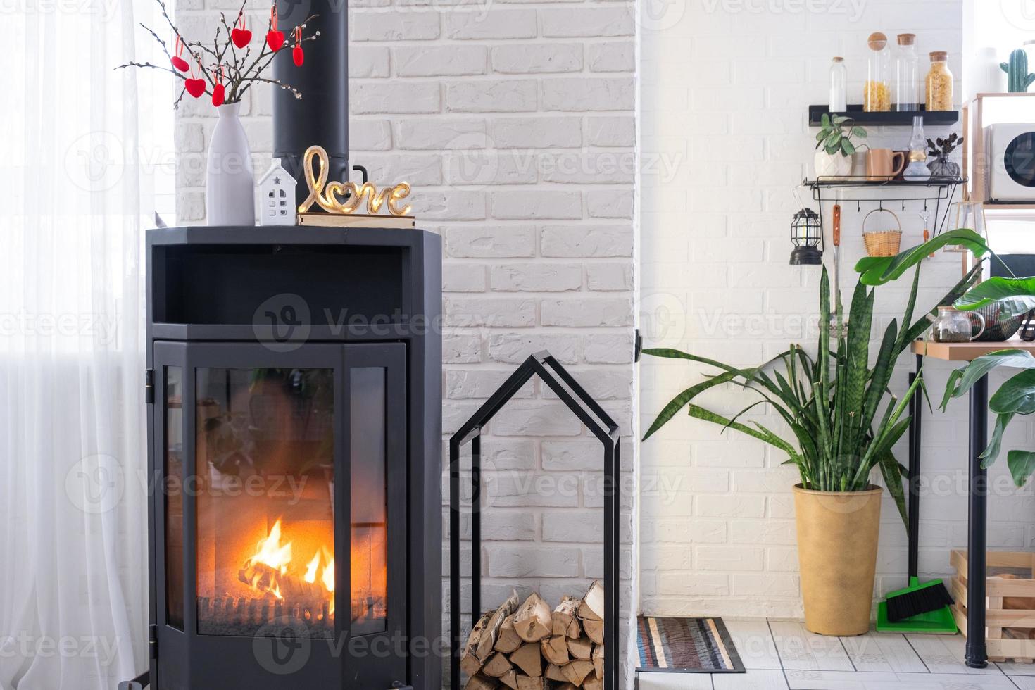 decoración de san valentín junto a la estufa de chimenea con fuego y leña. hogar acogedor en el interior con planes en maceta, día de san valentín en nido de amor familiar. foto