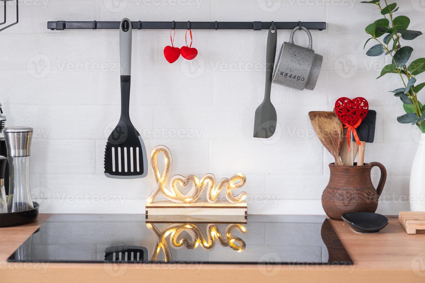The interior of the kitchen in the house is decorated with red hearts for Valentine's Day. Decor on the table, stove, utensils, festive mood in a family nest photo