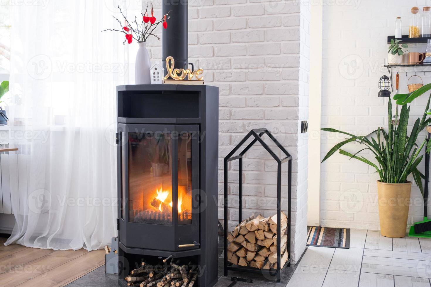 Valentine decor near fireplace stove with fire and firewood. Cozy home hearth in interior with potted plans, valentines day in family love nest. photo