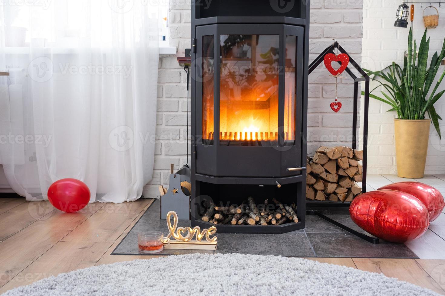Valentine decor near fireplace stove with fire and firewood. Cozy home hearth in interior with potted plans, valentines day in family love nest. photo