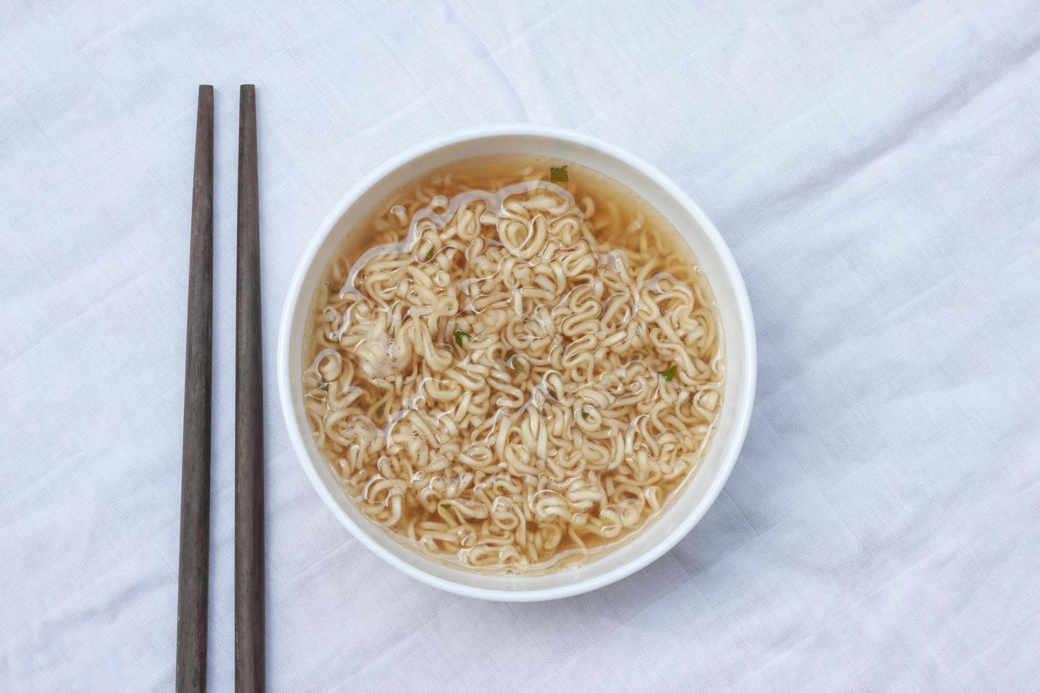 Top view of Instant noodles in a white bowl and chopsticks on a white tablecloth. photo