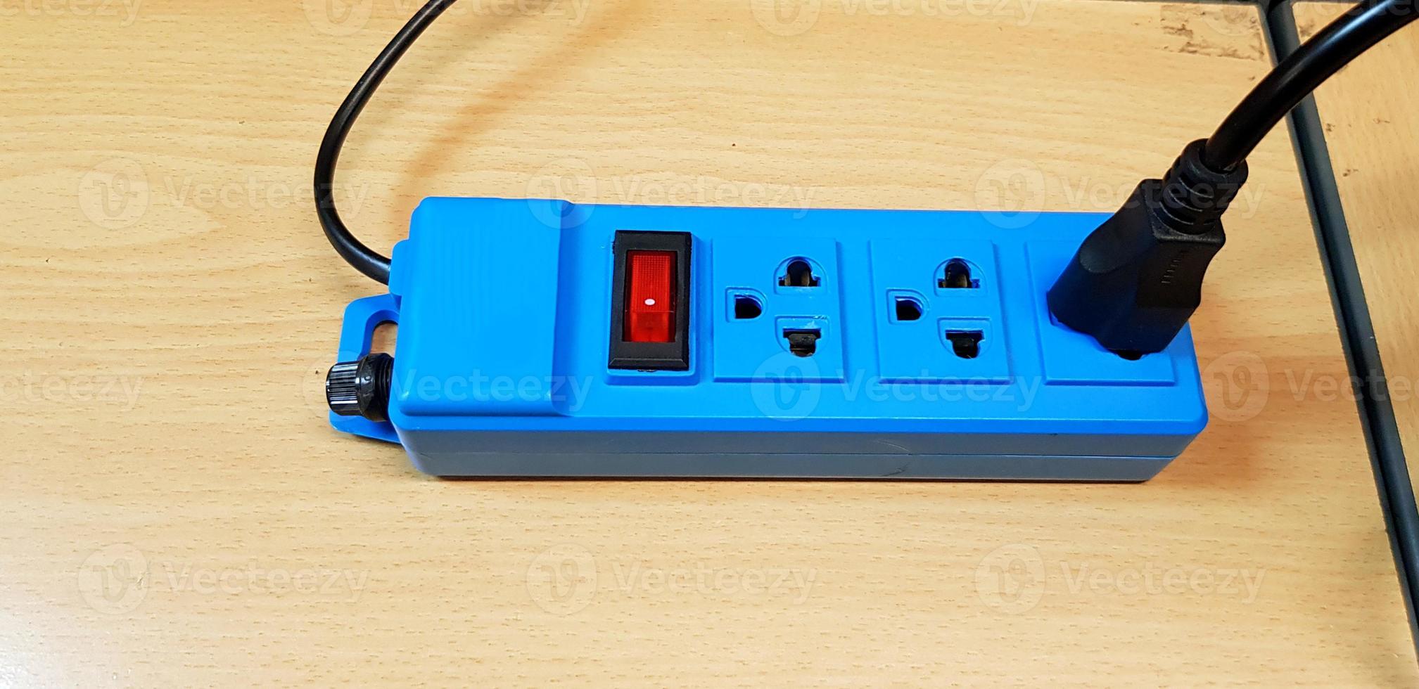 Blue AC outlet with red button or switch on or off and black power cord cable connect putting on wooden table photo