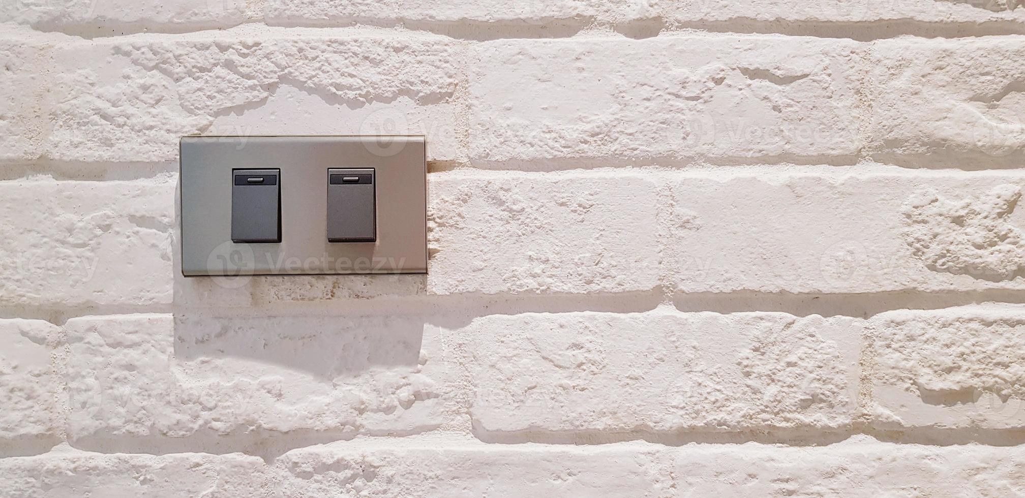 Gray light switch button installed on white rough or vintage wall with right copy space. Electricity, Electrical equipment and Background concept photo