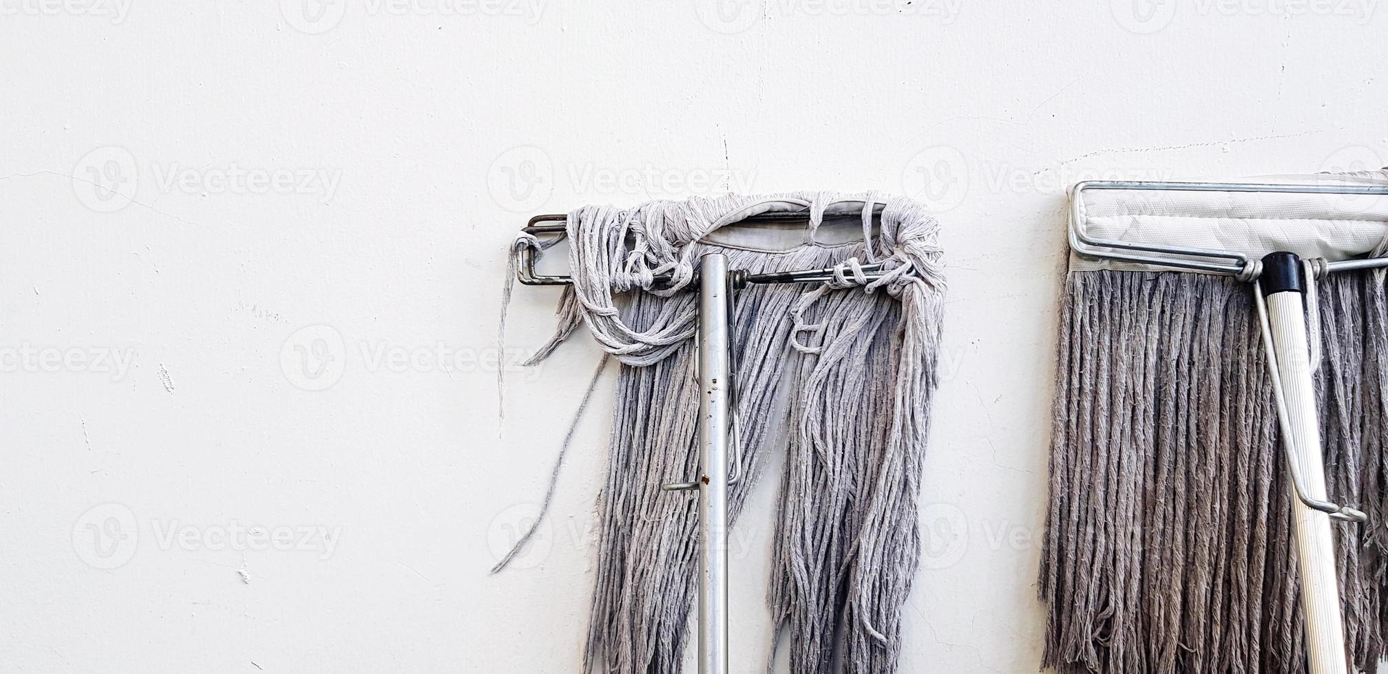 Two mops for cleaning floor and house leaning or isolated on white concrete wall with left copy space. Tool, Object, and Cleaner equipment concept photo