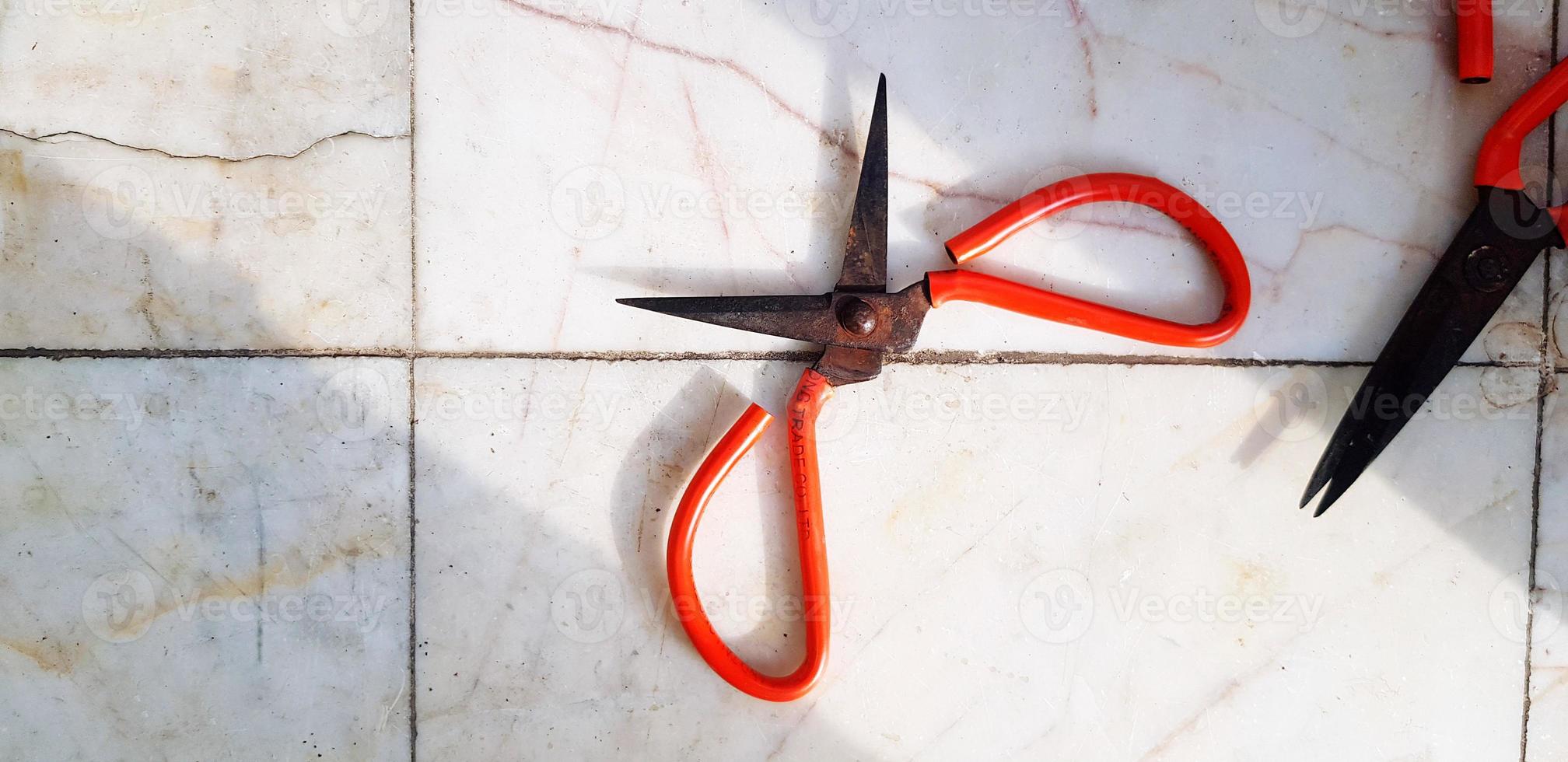 Two old red rusty scissors putting on white marble floor or background with copy space. Vintage object with sunlight shinning from beside photo