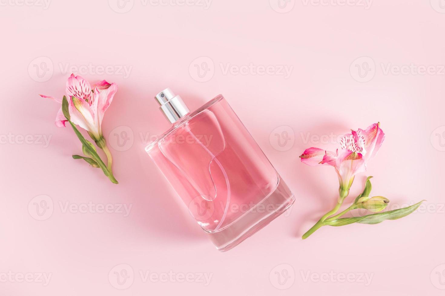 una botella transparente de producto cosmético, eau de parfum o spray de primer plano sobre un fondo rosa con capullos de flores de primavera. publicidad de productos foto