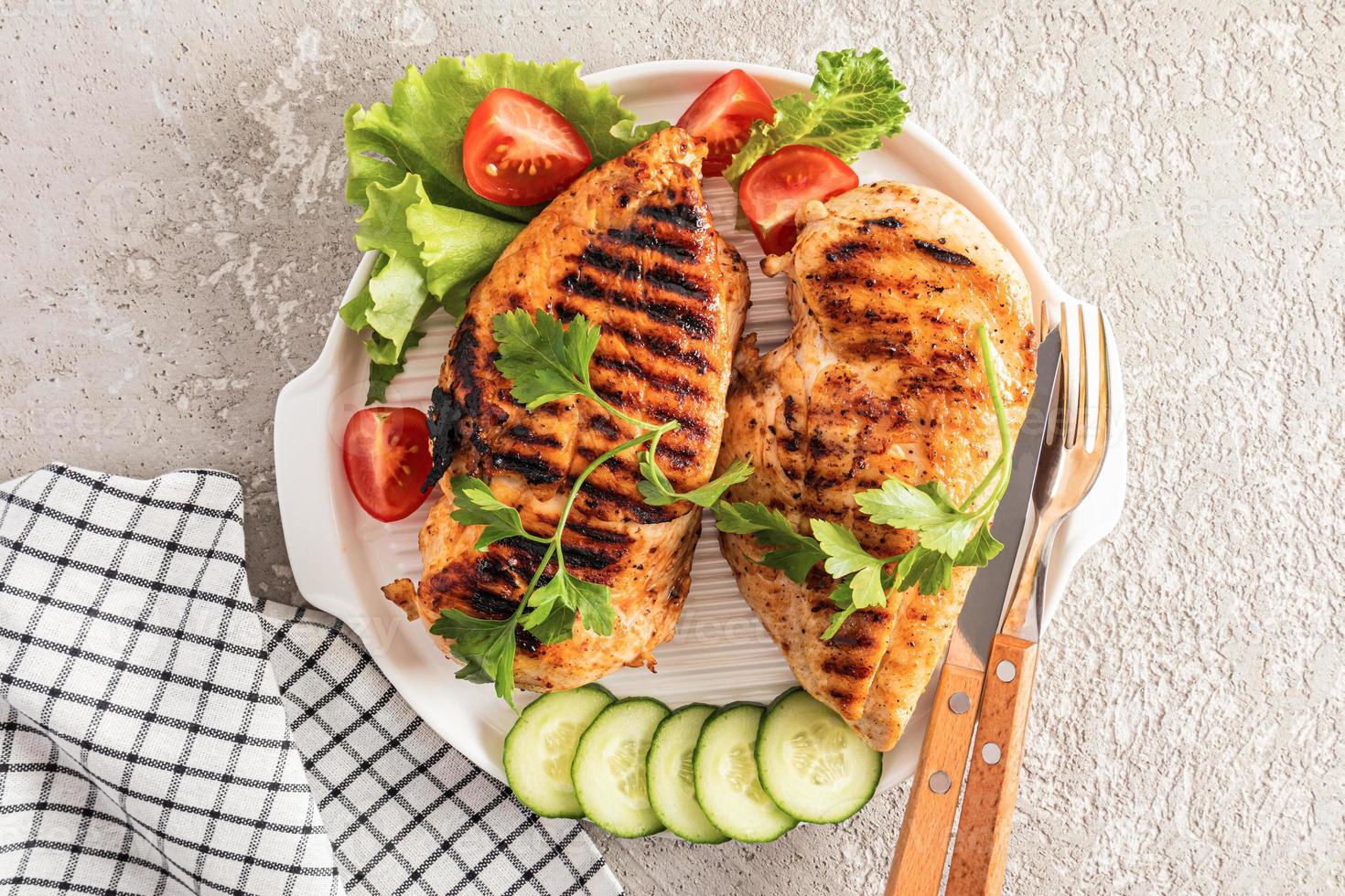 top view of a large serving plate with two breasts of grilled chicken fillet with fresh vegetables. gray cement background. menu. photo