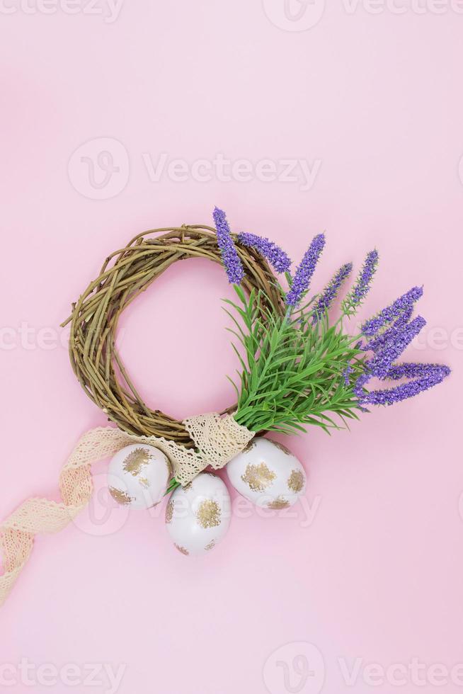 Painted white and gold eggs near wooden nest of branches with bouquet of lavender and string on pink background. View from above. Easter. Copy space photo