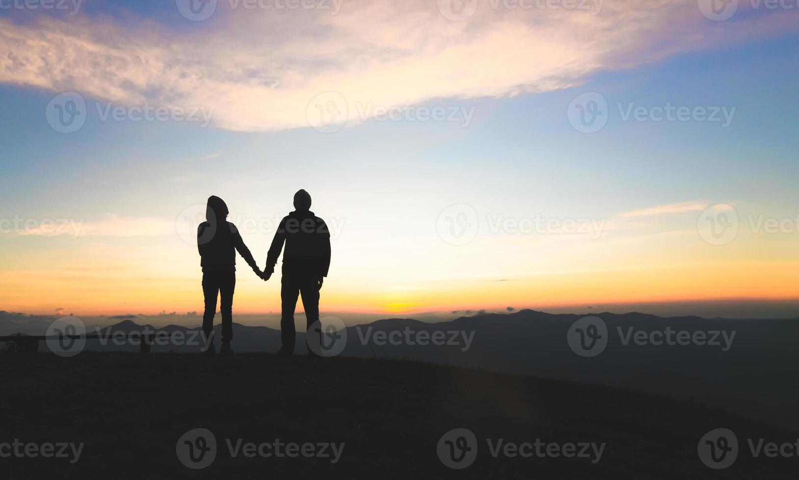 Silhouette of a couple on the mountain, A young romantic couple enjoy a beautiful view of the sun setting over the mountains, love, Valentine's Day. photo