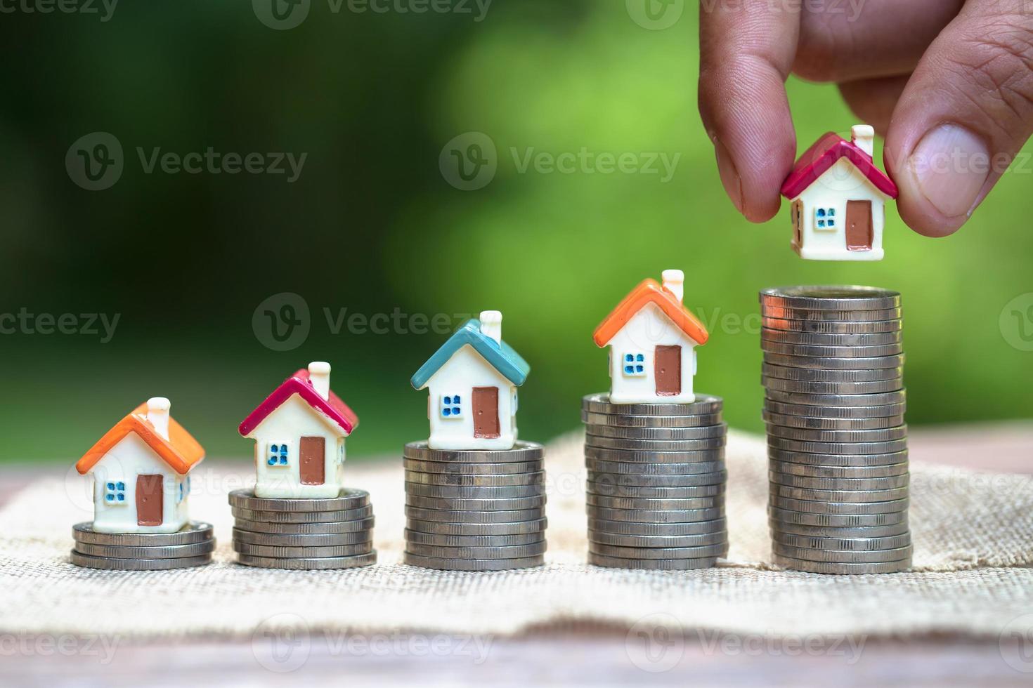 Human hand putting house model on coins stack. Concept for property ladder, home and residence, mortgage and real estate investment. photo