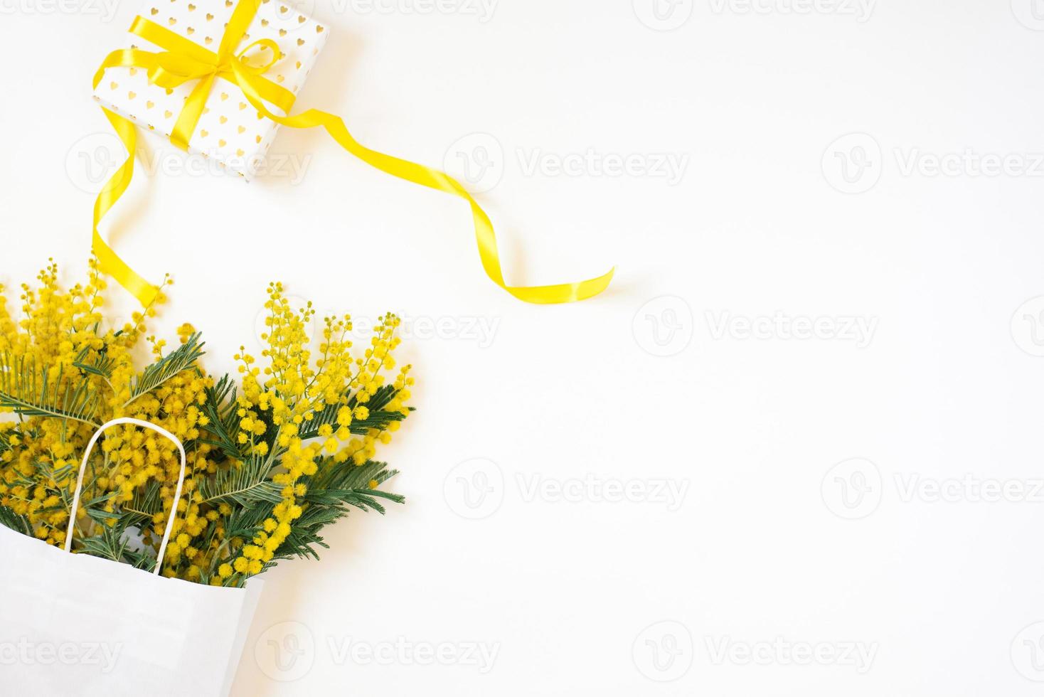 Beautiful flowers with package and present composition. Branches flowers mimosa on white background. Valentines Day, Easter, Birthday, Mother's day. Flat lay, top view, copy space photo