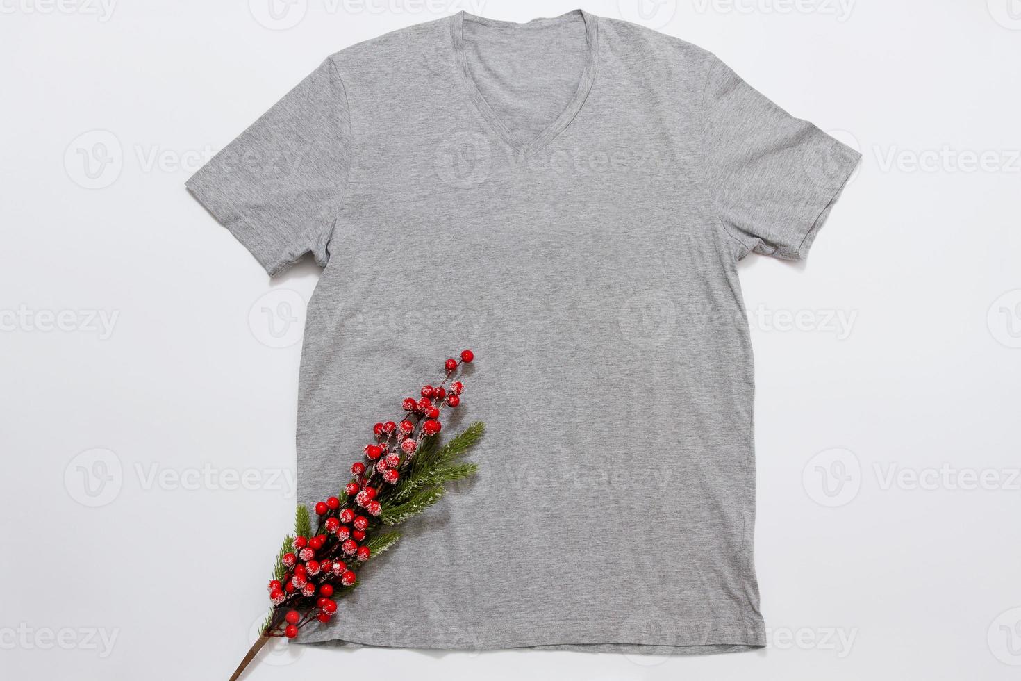 Close up grey blank template t shirt with copy space and Christmas Holiday concept. Top view mockup t-shirt and red holidays decorations on white background. Happy New Year accessories. Xmas outfit photo