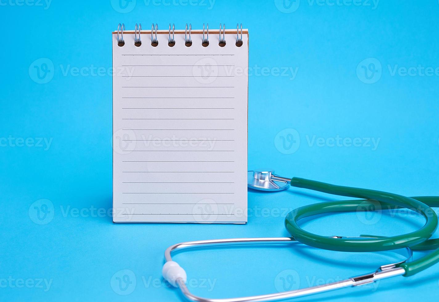 green medical stethoscope and empty paper notebook photo