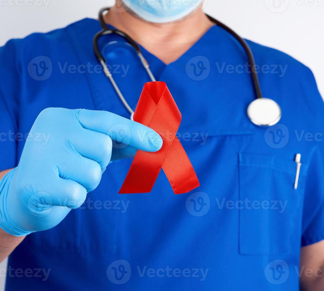 doctor in blue uniform and sterile latex gloves holds a red ribbon photo