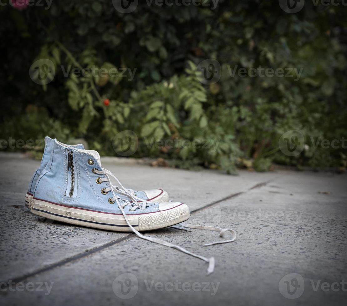 pair of old worn blue textile sneakers on gray asphalt photo