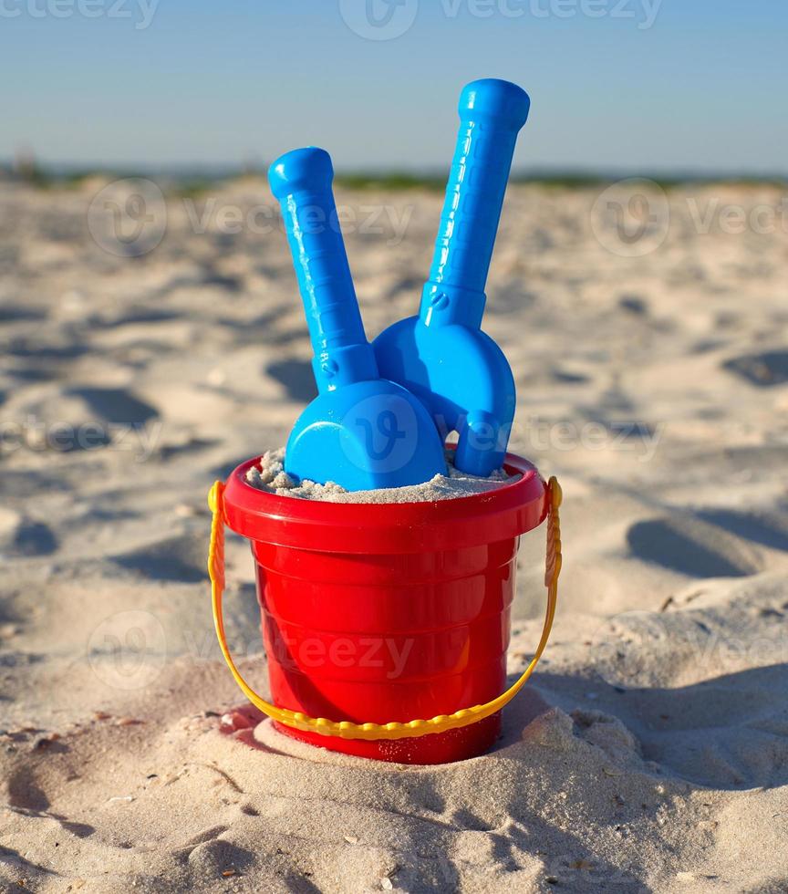 red plastic bucket and blue rake, shovel on the sand photo