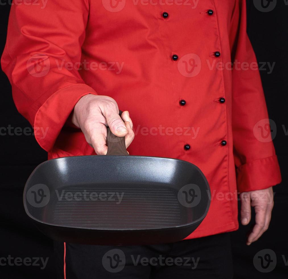 cook in red uniform holding an empty square black frying pan photo