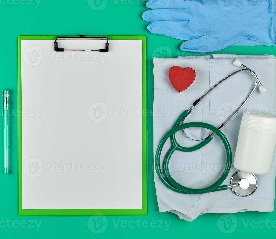 paper holder with empty white sheets, medical stethoscope, pills on a green background photo